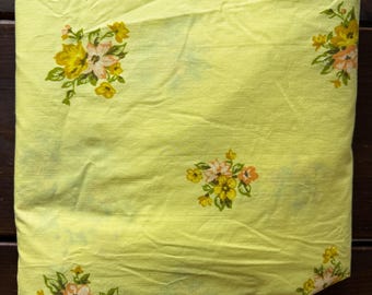 Pode incluir: Tecido amarelo dobrado com um padrão floral. As flores são em tons de amarelo, pêssego e branco, com folhas verdes. O tecido está dobrado e parece ser um lençol ou outro tipo de roupa de cama.