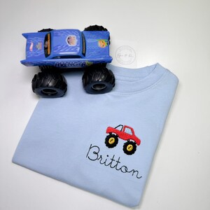 May include: Light blue t-shirt with an embroidered red monster truck and the name Britton.
