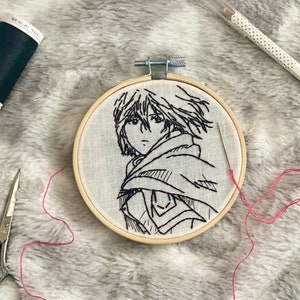 May include: A close-up of a completed embroidery hoop with a black and white line drawing of an anime character. The hoop is on a white fluffy surface with a needle, scissors, and spools of thread in various colors.
