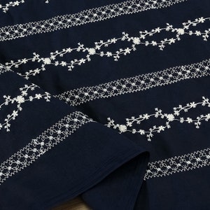 May include: Navy blue fabric with white embroidered floral patterns. The fabric is folded in half, showing the pattern on both sides.