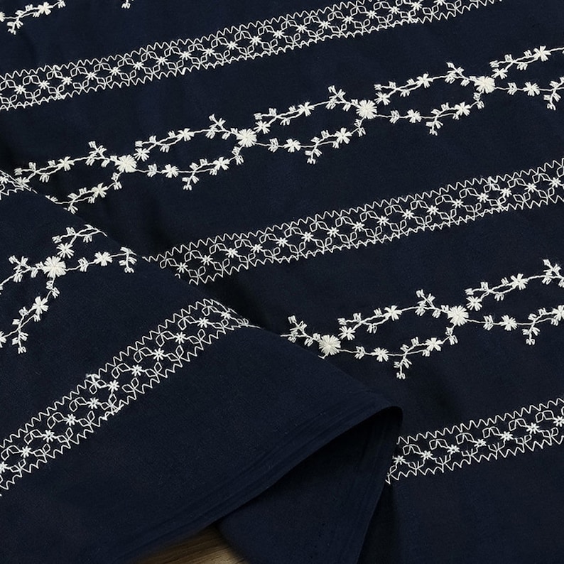 May include: Navy blue fabric with white embroidered floral patterns. The fabric is folded in half, showing the pattern on both sides.