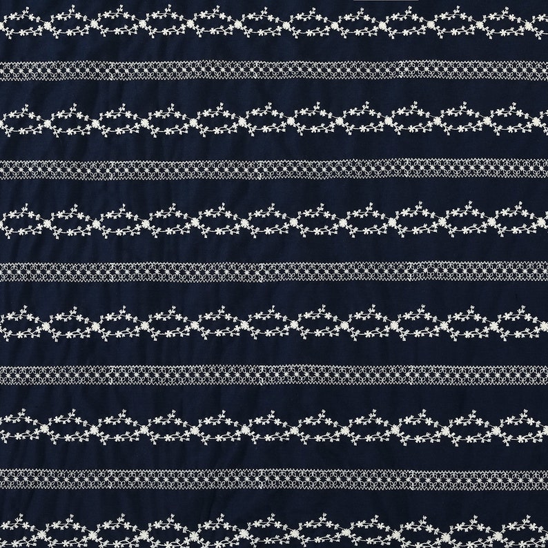 May include: A navy blue fabric with white embroidered floral patterns. The fabric has a repeating pattern of delicate floral vines with small white flowers.