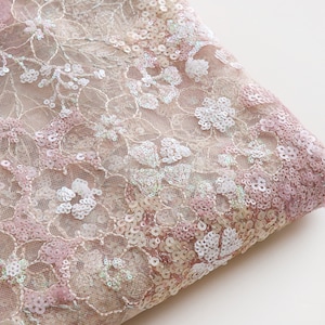 May include: Pink and white sequined lace fabric with a floral pattern. The fabric is delicate and has a soft, shimmery finish.