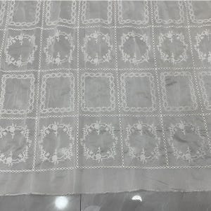May include: A sheer light gray fabric featuring a repeating grid pattern of white embroidered rectangles and circular floral wreaths. The embroidery is delicate and creates a structured geometric design across the translucent textile surface.