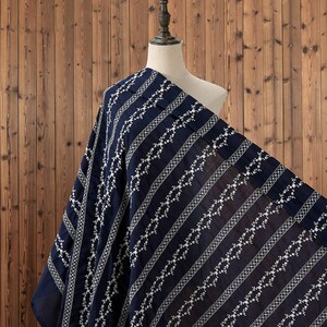 May include: Navy blue fabric with a white embroidered geometric pattern. The fabric has a striped design with a repeating pattern of white diamonds and lines.