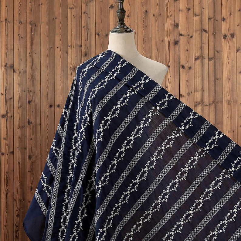 May include: Navy blue fabric with a white embroidered geometric pattern. The fabric has a striped design with a repeating pattern of white diamonds and lines.