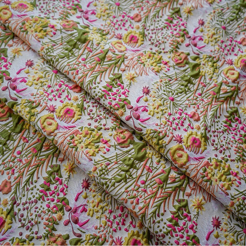 May include: White fabric with a floral pattern in shades of pink, yellow, and green. The fabric has a textured, raised design.