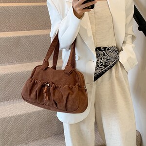 May include: A brown corduroy handbag with a drawstring closure and a silver accent. The bag has a structured shape and a top handle.