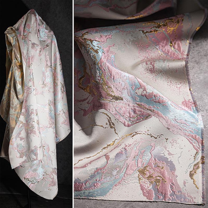 May include: A white fabric with a pink, blue, and gold marbled pattern. The fabric has a textured, woven look.
