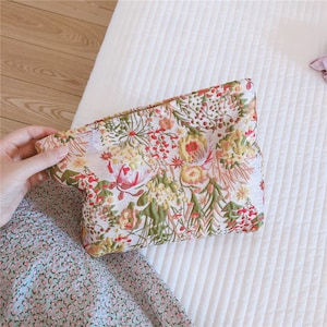 May include: A white floral clutch bag with a colourful floral pattern. The clutch is made of a textured fabric and has a zip closure.