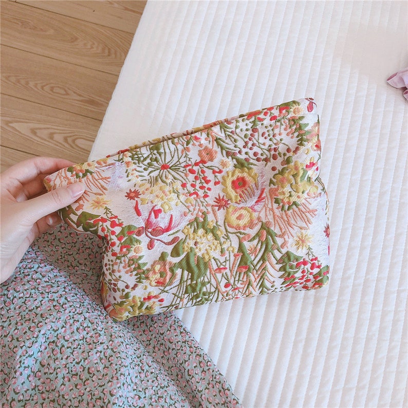May include: A white floral clutch bag with a colourful floral pattern. The clutch is made of a textured fabric and has a zip closure.