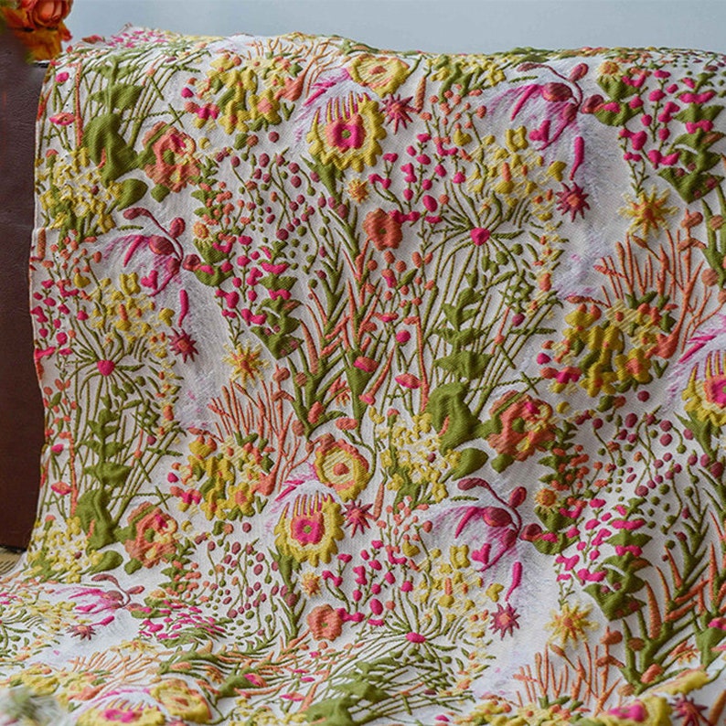 May include: White fabric with a floral pattern in shades of green, pink, yellow, and orange. The flowers are raised and textured, giving the fabric a 3D effect.