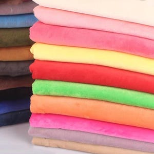 May include: A stack of colourful fabric swatches in various shades of pink, yellow, red, green, orange, purple, brown, and blue. The fabric is soft and plush, with a velvety texture.