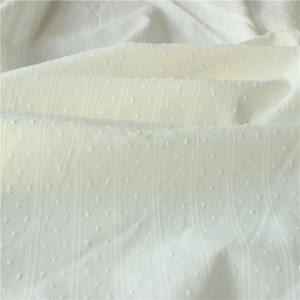 May include: White cotton fabric with a textured, dotted pattern and vertical stripes. The fabric is soft and lightweight, making it ideal for a variety of sewing projects.