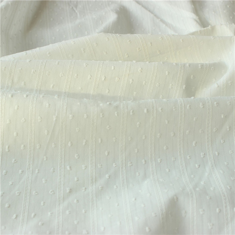 May include: White cotton fabric with a textured, dotted pattern and vertical stripes. The fabric is soft and lightweight, making it ideal for a variety of sewing projects.
