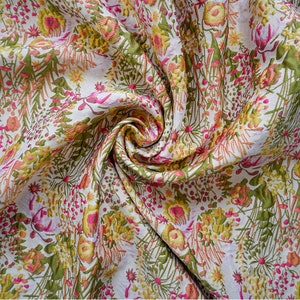 May include: A white fabric with a floral pattern in shades of pink, yellow, and green. The fabric is textured and has a slightly raised design.