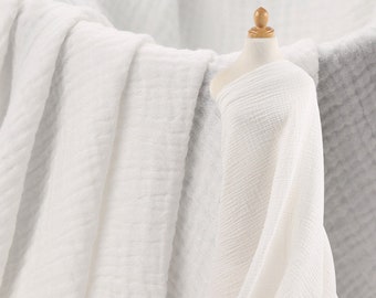 May include: White cotton gauze fabric with a textured, crinkled surface. The fabric is folded and draped over a mannequin.