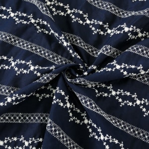 May include: Navy blue fabric with white embroidered floral patterns. The fabric is folded and shows the repeating pattern.