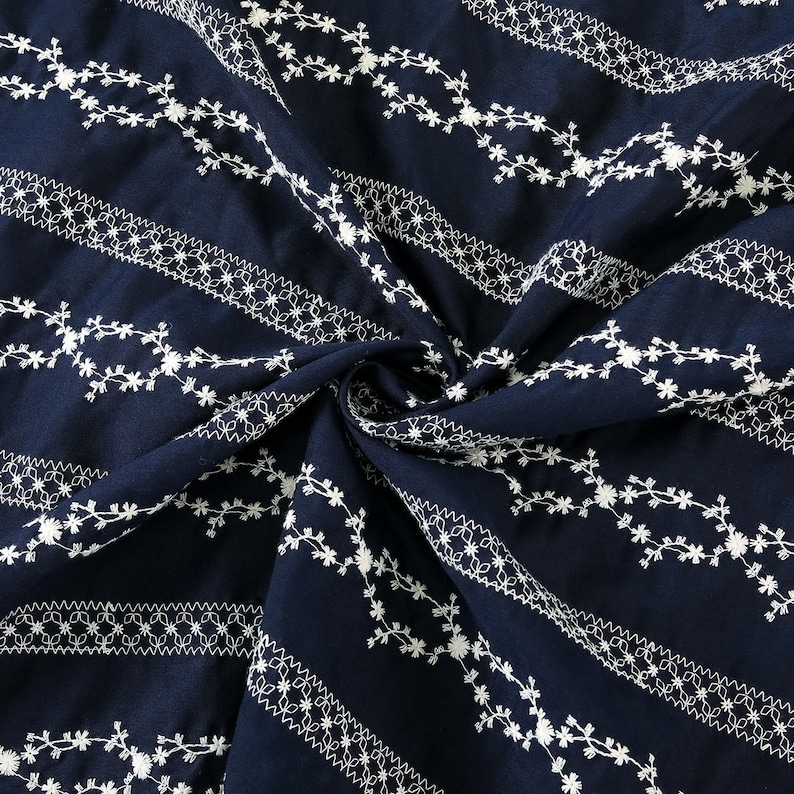 May include: Navy blue fabric with white embroidered floral patterns. The fabric is folded and shows the repeating pattern.
