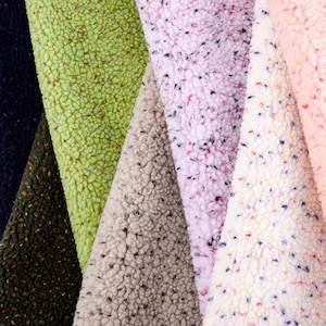 Könnte beinhalten: Nahaufnahme von fünf verschiedenen Stoffproben. Die Proben sind alle aus einem weichen, flauschigen Material mit einem gesprenkelten Muster. Die Farben der Proben sind grün, beige, rosa, weiß mit roten und blauen Sprenkeln und weiß mit gelben und blauen Sprenkeln.