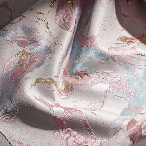 May include: A close-up of a fabric with a pink, blue, and gold marble pattern. The fabric is soft and has a subtle sheen.