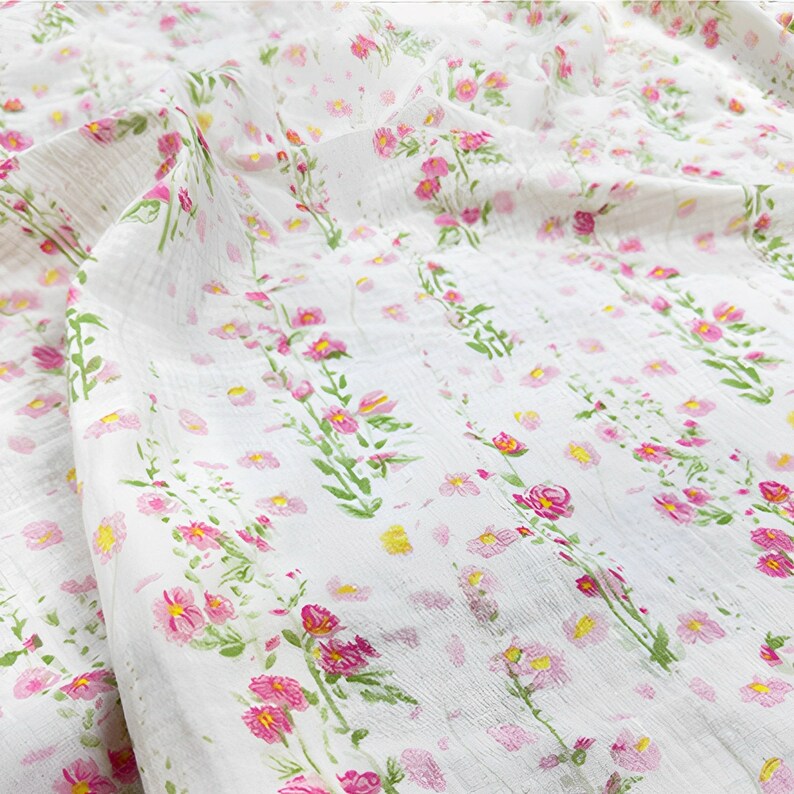 May include: White fabric with a pink floral print. The fabric features small pink flowers and larger pink flowers with green stems.