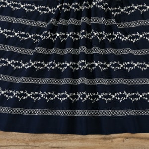 May include: Navy blue fabric with white embroidered floral patterns. The fabric has a repeating pattern of delicate floral vines and small flowers.