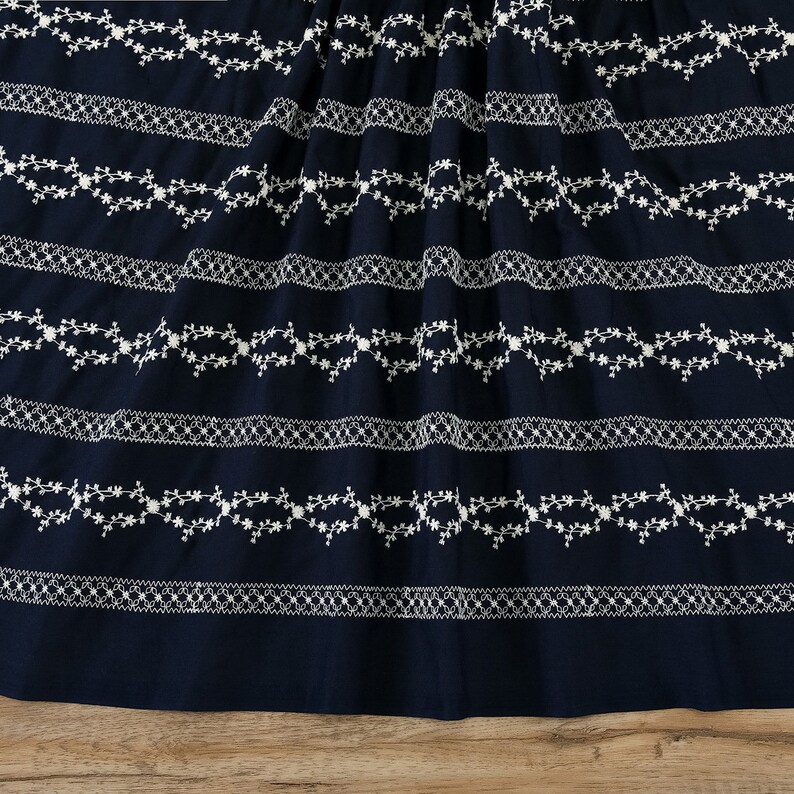 May include: Navy blue fabric with white embroidered floral patterns. The fabric has a repeating pattern of delicate floral vines and small flowers.