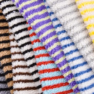 May include: A close-up of a variety of striped fabrics in different colors, including black and white, red and blue, purple and yellow, and gray. The fabrics are soft and fluffy, and they are arranged in a way that shows off their different textures.