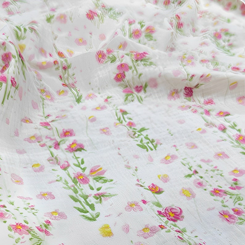 May include: White sheer fabric with a delicate floral pattern in shades of pink and green. The fabric has a subtle texture and a soft, flowing drape.