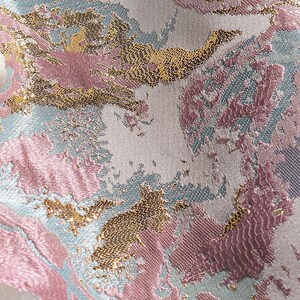 May include: Close-up of a fabric with a pink, gold, and blue abstract pattern. The fabric has a textured, woven look.