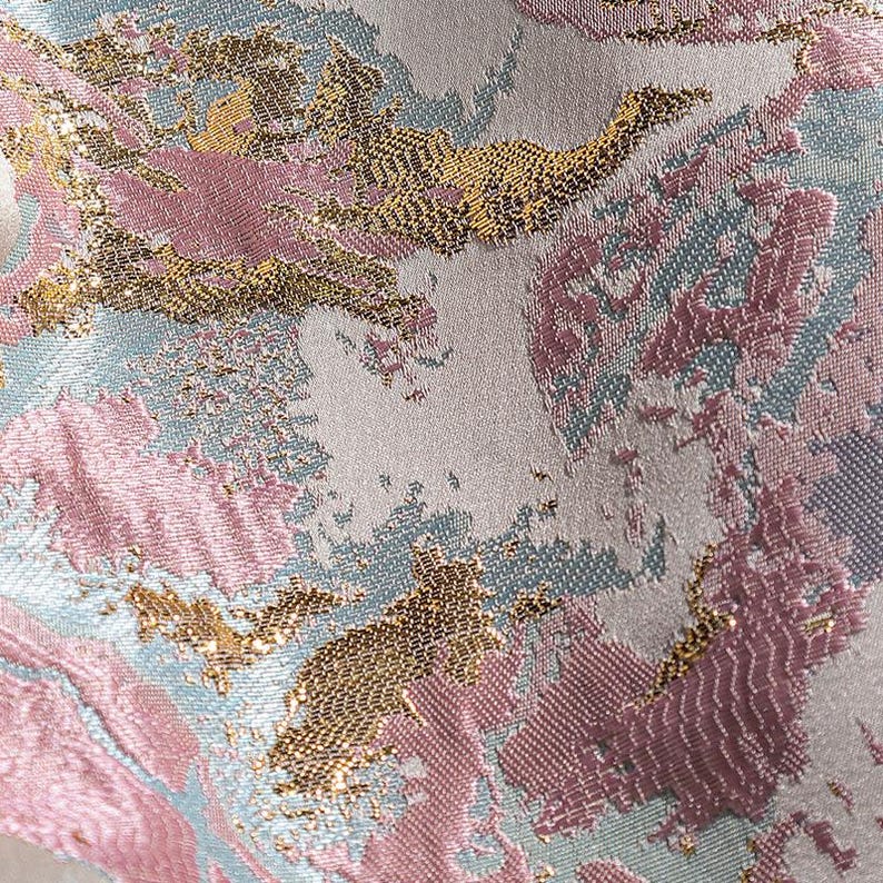 May include: Close-up of a fabric with a pink, gold, and blue abstract pattern. The fabric has a textured, woven look.