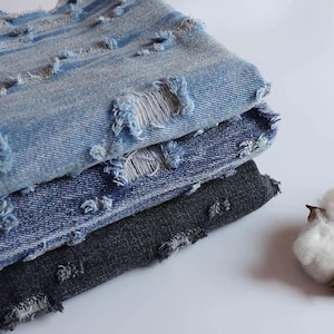 May include: A stack of three distressed denim fabrics. The top fabric is light blue, the middle fabric is a darker blue, and the bottom fabric is black.
