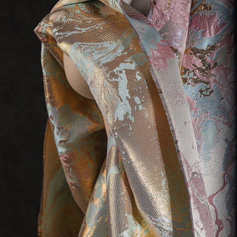 May include: Close-up of a fabric with a metallic sheen and a marbled pattern in shades of gold, pink, and blue.