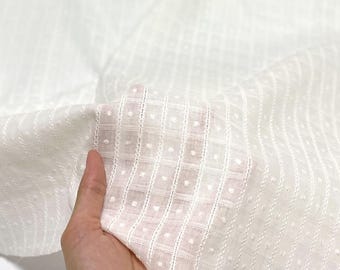 May include: Close-up of white fabric with a delicate, textured pattern. The fabric features a grid-like design with small, raised dots within each square. The material appears lightweight and semi-sheer, ideal for clothing or home decor.