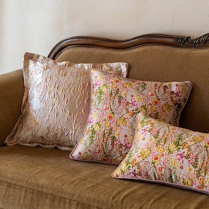 May include: Three decorative throw pillows on a brown sofa. The pillow at the back is a light pink with a textured pattern. The two pillows at the front are pink with a floral pattern.