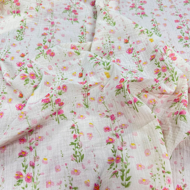 May include: White fabric with a pink floral print. The fabric has a textured, gauze-like appearance.