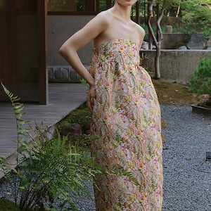 May include: A strapless maxi dress with a floral print in shades of pink, yellow, and green. The dress has a fitted bodice and a flowing skirt.