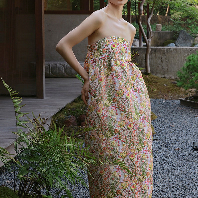 May include: A strapless maxi dress with a floral print in shades of pink, yellow, and green. The dress has a fitted bodice and a flowing skirt.