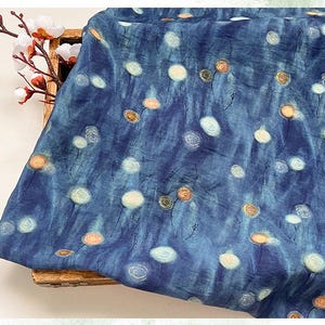 May include: A piece of blue fabric with a pattern of white and orange floral designs. The fabric has a textured appearance and a watercolor-like effect. The floral pattern is scattered across the fabric.