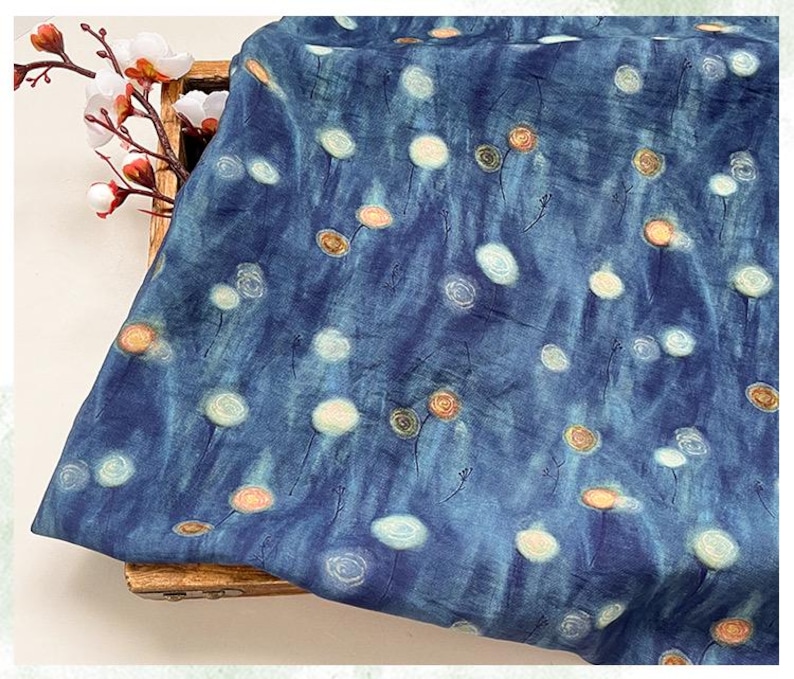 May include: A piece of blue fabric with a pattern of white and orange floral designs. The fabric has a textured appearance and a watercolor-like effect. The floral pattern is scattered across the fabric.