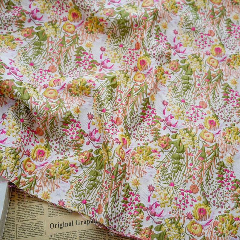 May include: White fabric with a floral pattern in shades of pink, yellow, and green. The fabric has a textured, raised surface.