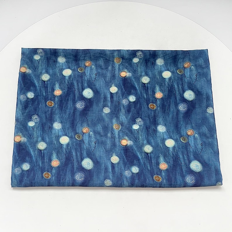 May include: A rectangular fabric with a dark blue background and a pattern of white, light orange, and brown floral designs. The fabric has a watercolor-like appearance, with soft, blended colors.