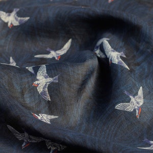 Puede incluir: Una tela azul oscuro con un patrón de pájaros blancos. Los pájaros vuelan en diferentes direcciones. La tela tiene una textura sutil.