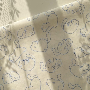 Peut inclure: Tissu blanc cassé avec un motif répétitif d'illustrations de chats bleus. Les chats sont représentés dans diverses poses ludiques, comme couchés sur le dos ou enroulés. Le tissu a un aspect doux et légèrement texturé.