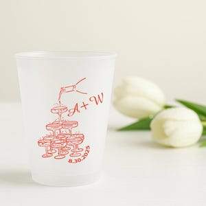 Puede incluir: Un vaso de plástico esmerilado con una ilustración roja de copas de champán apiladas en pirámide, con una botella vertiendo champán. El vaso tiene las iniciales "A + W" y la fecha "8.30.2025" impresas en rojo.