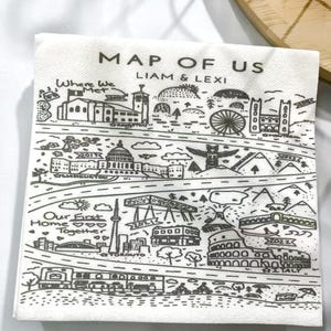 May include: White napkin with a black illustrated map design. The map includes landmarks, roads, and text that reads "MAP OF US", "LIAM & LEXI", and locations like "TORONTO" and "ITALY".