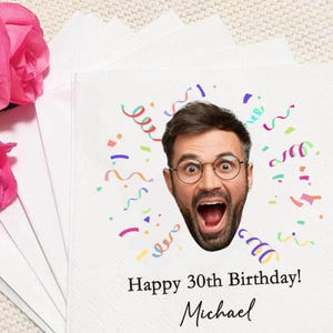 Könnte beinhalten: Weiße Papierservietten mit einem Aufdruck. Das Design zeigt das Gesicht eines Mannes mit Brille und offenem Mund, umgeben von bunten Konfetti und Luftschlangen. Der Text lautet "Happy 30th Birthday! Michael."