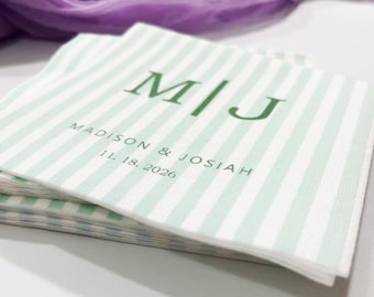 May include: A stack of white and light green striped napkins. The napkins are printed with the initials "M|J", the names "Madison & Josiah", and the date "11. 18. 2026" in green lettering. A purple fabric is in the background.
