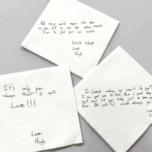 Könnte beinhalten: Drei weiße Papierservietten mit handgeschriebenen Nachrichten in schwarzer Tinte. Die Nachrichten enthalten Sätze wie "Smile always" und "Love!!!". Die Servietten sind auf einer hellgrauen Oberfläche angeordnet.